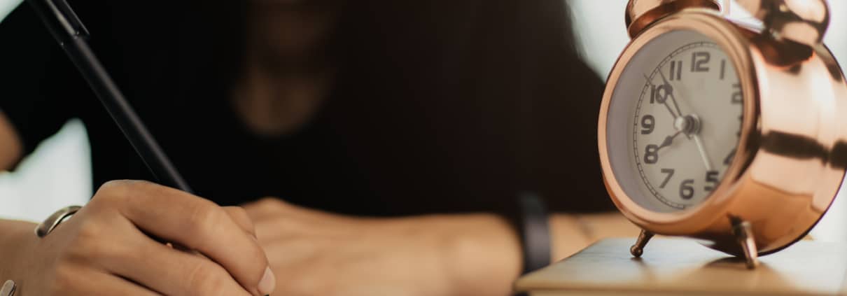 woman writing notebook with alarm-clock