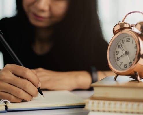 woman writing notebook with alarm-clock